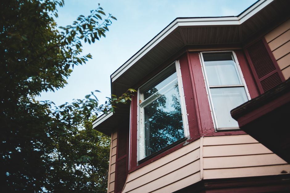 From below of cozy residential cottage with geometric facade and windows reflecting green trees and sky