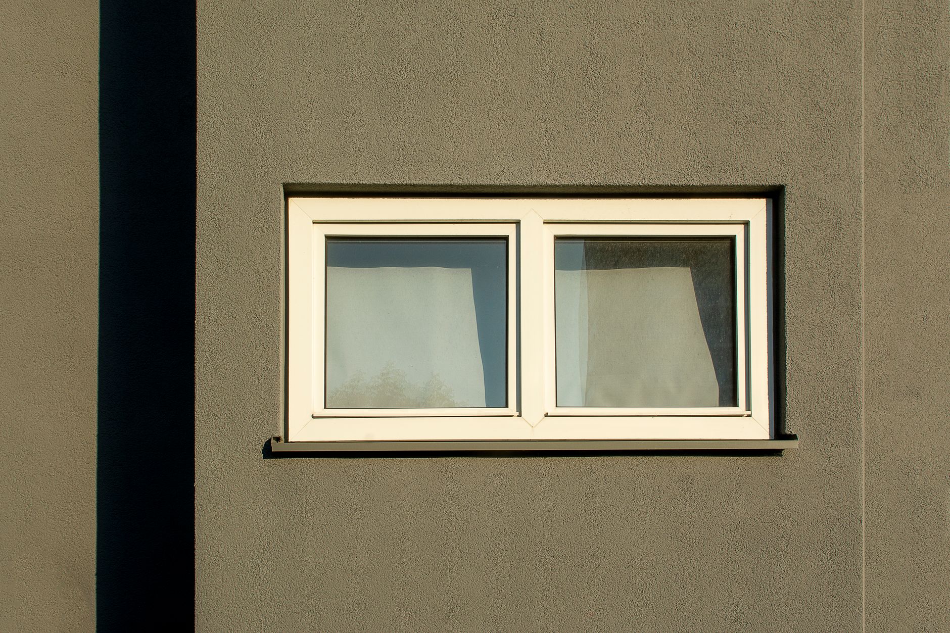 A minimalist white window on a textured concrete wall casting shadows in sunlight in Riverside, CA